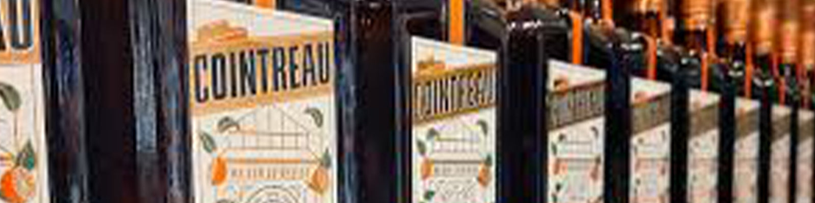 A row of Cointreau bottles lined up on a shelf, each with a distinct label displaying the brand name and decorative elements. The bottle caps are a copper color, adding a touch of elegance.