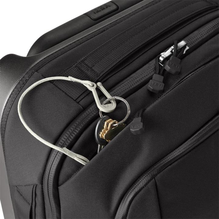 A Yeti - Crossroads - Luggage 22 in black, featuring a visible zipper pull and keys secured by a plastic cord lock. This bag offers multiple compartments, including a slightly open pocket revealing the keys on a ring.