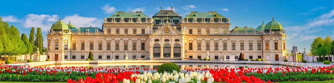 The image shows a grand palace with a symmetrical design, featuring green domes and a large courtyard. In the foreground, there are colorful blooming tulips and a reflecting pool, with a bright blue sky above.