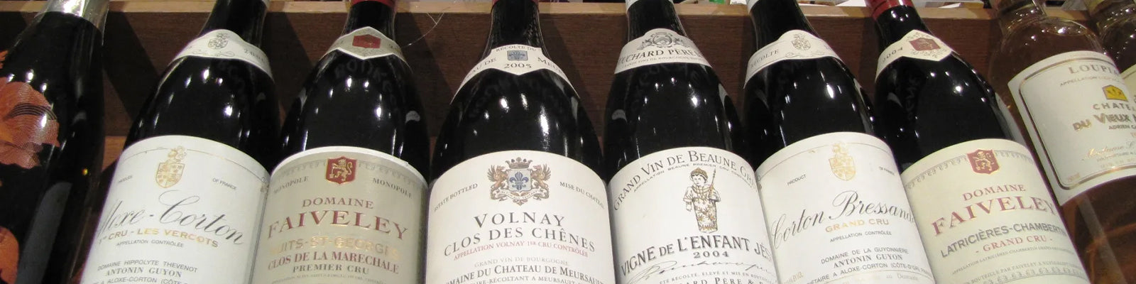 Eine Reihe von Rotweinflaschen in einem Regal. Auf den Etiketten stehen Namen wie Domaine Faiveley, Volnay Clos des Chênes und Pommard Premier Cru. Die Flaschen variieren in Jahrgang und Herkunft.