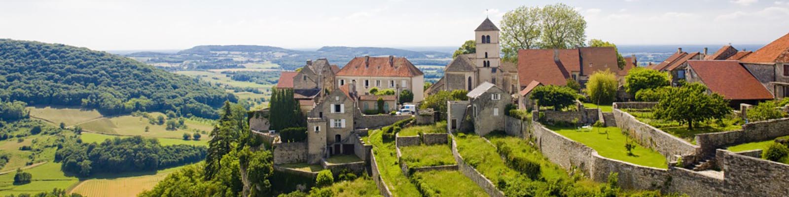 Ein malerischer Blick auf ein malerisches Dorf mit Steinhäusern und einer Kirche, umgeben von üppig grünen Hügeln und Landschaften unter einem klaren blauen Himmel.