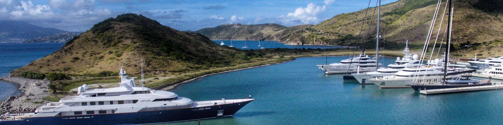 Scenic view of yachts docked in a serene bay surrounded by green hills under a clear blue sky.