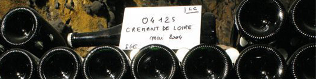 Wine bottles stacked horizontally in a dimly lit cellar. A label reads 04125 Crémant de Loire, indicating the type of wine.