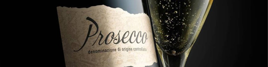 Primer plano de una botella de prosecco con la etiqueta visible junto a una copa llena de prosecco espumoso. La copa está inclinada, mostrando las burbujas que suben a la superficie sobre un fondo oscuro.