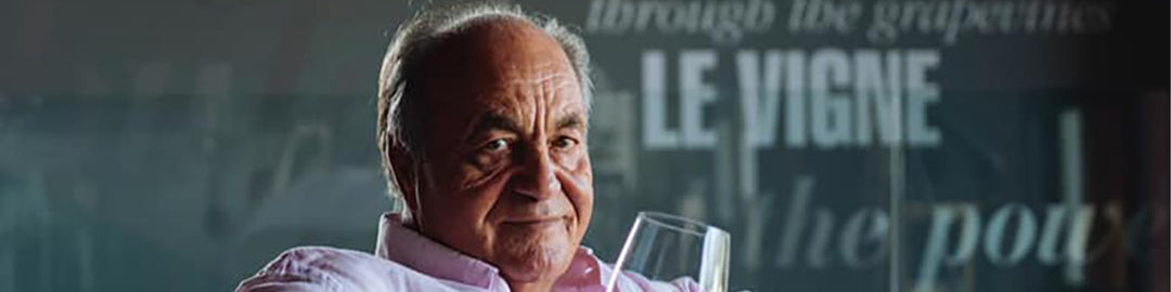 A person in a pink shirt holds a wine glass, sitting in front of a backdrop with the word Le Vigne partially visible.