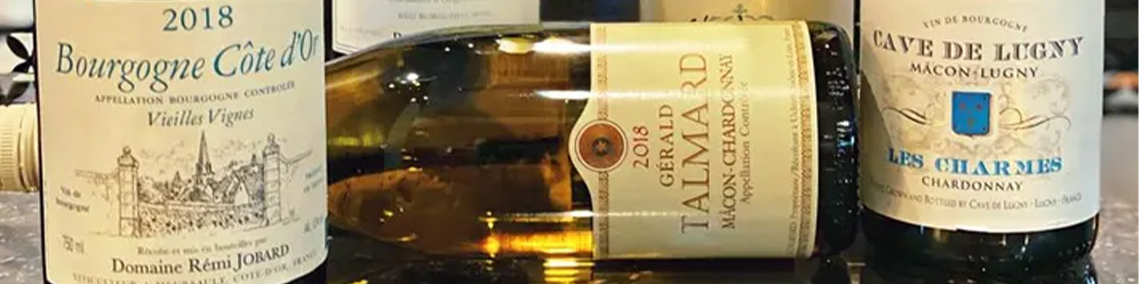 A selection of three Chardonnay wine bottles, including Domaine Remi Jobard, Gérald Talmard Mâcon-Chardonnay, and Cave de Lugny Les Charmes, displayed on a table.