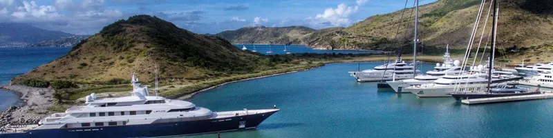 Yachts docked in a serene bay surrounded by green hills under a clear blue sky