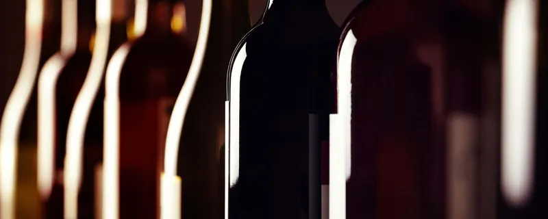 Wine bottles in dim lighting, their silhouettes and reflections along the glass